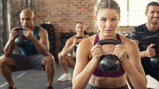 A group of people gathers around a kettlebell, engaged in a dynamic workout session. They demonstrate proper form and coordination, reflecting teamwork and dedication to fitness goals