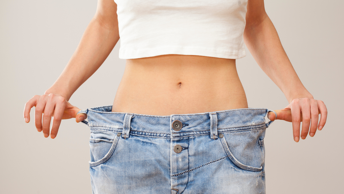 a photo of a woman showcasing her weight loss by holding out her large old jeans away from her new, slimmer figure